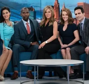 Cinco pessoas posam formalmente em sofá azul num estúdio de TV com skyline. Três mulheres e dois homens, um fotógrafo à esquerda.