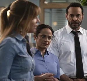 Em um escritório, um homem sério de gravata e mulheres com expressões preocupadas olham para fora da cena. Clima tenso.