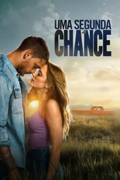 Um casal se abraça em campo com grama alta ao pôr do sol, um caminhão laranja ao fundo. Clima romântico e rural.