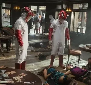 Duas figuras mascaradas em trajes brancos e vermelhos em saloon. Corpos estendidos no chão. Cenário caótico e violento.