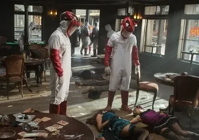 Duas figuras mascaradas em trajes brancos e vermelhos em saloon. Corpos estendidos no chão. Cenário caótico e violento.