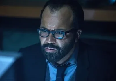 Um homem de barba e óculos olha intensamente para uma tela azulada. O ambiente escuro sugere foco e tensão.
