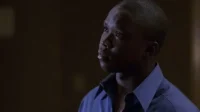 Jovem negro de camisa azul,olhando para cima com expressão pensativa. Fundo escuro e difuso cria um clima sombrio.