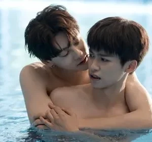 Dois jovens sem camisa se abraçam numa piscina. Um sussurra no ouvido do outro, que tem uma expressão surpresa e intensa.