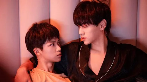 Amor Vingado – T01E17:Se o ódio é profundo demais,não tem espaço pro amor crescer 1 Dois homens jovens sentados,um em roupão preto abraça o outro,que o encara intensamente. A luz avermelhada e o fundo suave criam um clima íntimo.