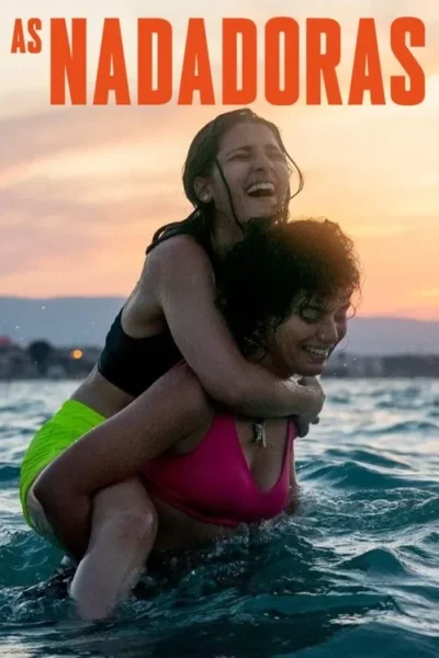 Duas mulheres sorridentes e molhadas brincam na água. Uma carrega a outra nas costas, com um pôr do sol laranja ao fundo.
