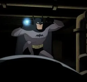 Figura mascarada de traje cinza e preto, com luz azul, espreita em área escura com tubulações. Clima tenso e misterioso.