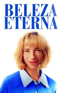 Close-up de mulher loira com cabelo curto e franja,sorrindo levemente. Ela veste camisa azul com colarinho claro sobre fundo branco.