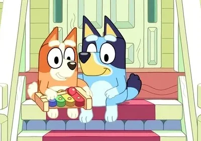 Dois cães animados sorridentes em degraus. O laranja toca um xilofone, o azul observa. Cenário doméstico vibrante e feliz.