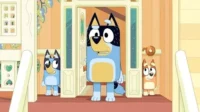 Um cachorro adulto azul e preto surpreso na porta, com dois filhotes, um curioso e outro tímido, espiando de trás.