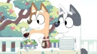 Dois cães animados preparam uma refeição ao ar livre. Um cão veste salada, enquanto o outro organiza pratos. Clima feliz.
