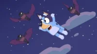Cão azul flutua assustado/surpreso no céu noturno estrelado. Três morcegos escuros com asas roxas voam entre nuvens.