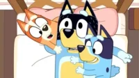 Três cães azuis e laranjas animados, um adulto e duas crianças, abraçando-se alegremente em uma cama.