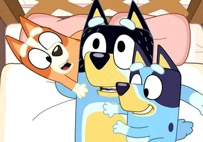 Três cães azuis e laranjas animados, um adulto e duas crianças, abraçando-se alegremente em uma cama.