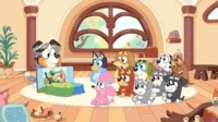 Cachorro adulto lê um livro pop-up para vários filhotes de raças diferentes, sentados numa sala aconchegante e iluminada. Clima de história e aprendizado.