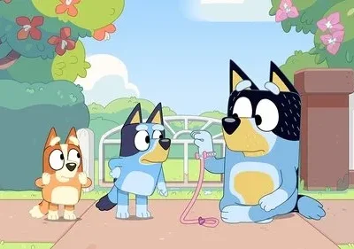 Três cães animados em uma calçada ensolarada. Um adulto azul segura uma guia rosa, enquanto dois filhotes laranja e azul observam.
