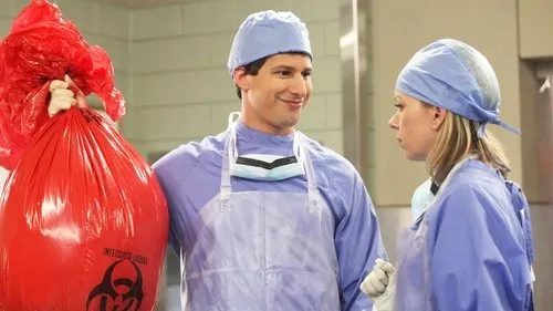 Brooklyn Nine-Nine:Lei e Desordem – T01E04:Novo relacionamento 1 Dois cirurgiões em uniforme azul. Um homem sorri maliciosamente segurando um saco de lixo vermelho de risco biológico. Uma mulher o olha séria.