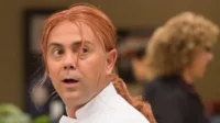 Um chef ruivo de jaleco branco, com expressão de surpresa, olhos arregalados e vesgos. Fundo desfocado.