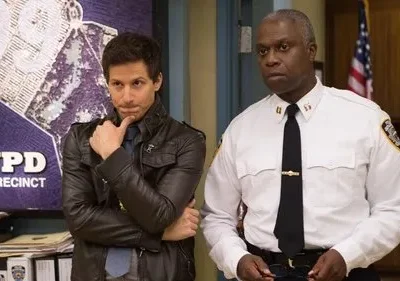 Um detetive jovem, pensativo em jaqueta de couro, ao lado de um oficial mais velho e sério em uniforme policial. Fundo de delegacia.