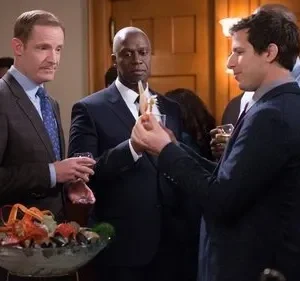 Três homens de terno em festa formal observam um pedaço de marisco. Um tacho com lagosta está na frente. Clima de humor e curiosidade.