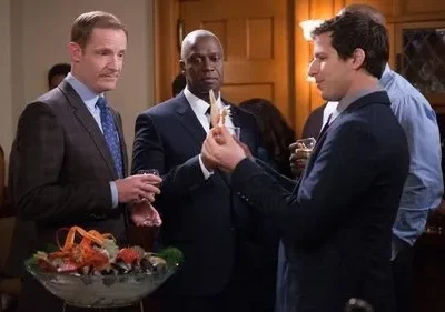 Três homens de terno em festa formal observam um pedaço de marisco. Um tacho com lagosta está na frente. Clima de humor e curiosidade.