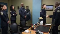 Seis policiais em uniforme azul numa sala. Dois homens sorriem ao apertar as mãos, enquanto quatro colegas os observam.