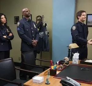Seis policiais em uniforme azul numa sala. Dois homens sorriem ao apertar as mãos, enquanto quatro colegas os observam.