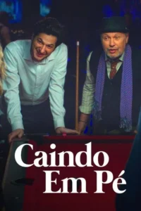 Dois homens,um jovem sorrindo e um mais velho sério com chapéu e cachecol roxo,encostados numa mesa de bilhar em bar.