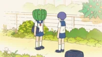 Duas colegiais ao ar livre. Uma tem uma abóbora verde na cabeça com olhos raivosos, a outra está de costas. Clima surreal e colorido.