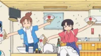 Duas figuras anime alegres dançam com leques japoneses e confetes em uma sala caótica. Uma pessoa dorme na mesa. Clima festivo e divertido.
