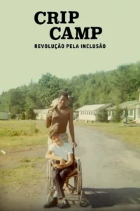 Foto vintage:Jovem negro empurra amigo branco sorrindo em cadeira de rodas,em acampamento sob sol. Clima de camaradagem.