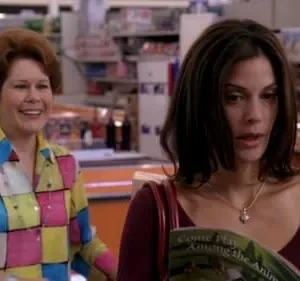 Duas mulheres em um mercado. Uma sorri com camisa colorida xadrez, a outra lê uma revista com expressão séria. Clima de cotidiano.