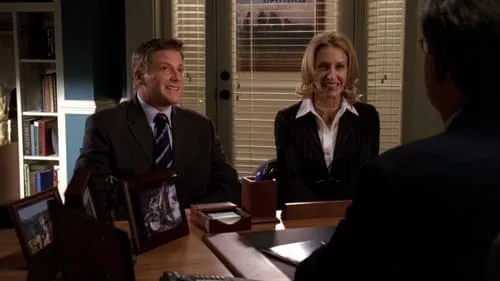 Dois executivos sorridentes,um homem e uma mulher,em uma mesa de escritório. Um terceiro de costas na frente. Ambiente profissional.