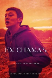 Homem em hoodie roxo sob céu vibrante de pôr do sol em tons de laranja e vermelho. Ele olha para cima com expressão intensa.