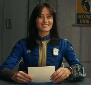 Mulher sorridente de uniforme azul e amarelo, com aparelho no pulso, segurando cartão. Fundo de bunker com pôster vintage.