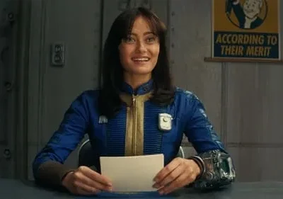 Mulher sorridente de uniforme azul e amarelo, com aparelho no pulso, segurando cartão. Fundo de bunker com pôster vintage.