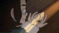 Jovem animado sorri, olhando uma aranha colorida nas suas mãos, iluminadas por um feixe de luz quente.