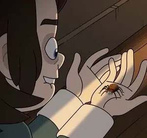 Jovem animado sorri, olhando uma aranha colorida nas suas mãos, iluminadas por um feixe de luz quente.