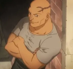 Homem careca e musculoso, com cicatrizes na cabeça e camiseta cinza, cruza os braços com um sorriso confiante em ambiente escuro.