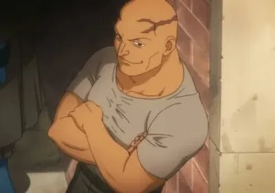 Homem careca e musculoso, com cicatrizes na cabeça e camiseta cinza, cruza os braços com um sorriso confiante em ambiente escuro.