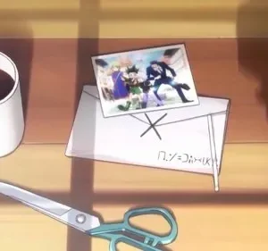 Mesa com caneca, tesoura e envelope. Uma foto mostra quatro personagens de anime: um de cabelo verde e um de terno, correndo. Sugere aventura e união.