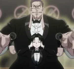 Homem imponente de terno com pontos no rosto e correntes nos dedos. Um jovem tapa os ouvidos à frente. Sinais de proibido no fundo. Clima misterioso.