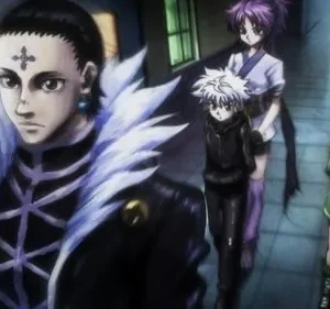 Um homem de gola bufante e cruz na testa lidera 4 figuras, incluindo jovens, em um corredor escuro e azulado. Clima tenso.