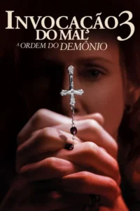 Close-up de mãos em oração segurando um terço com crucifixo invertido. Uma mulher de rosto sério desfocado ao fundo. Atmosfera sombria.