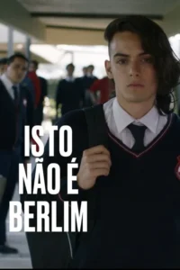 Jovem de uniforme escolar com cabelo longo de um lado e raspado do outro,olha sério para a câmera. Alunos ao fundo.