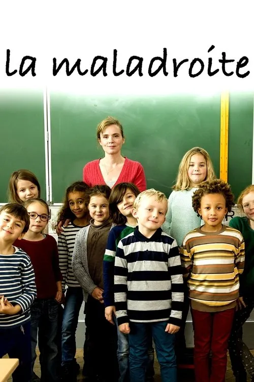 Uma professora e várias crianças de escola primária sorriem para a câmera em uma sala de aula,com um quadro verde ao fundo.