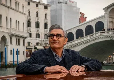 Homem de óculos, cabelo grisalho, em um barco em Veneza, olhando para o lado. Ao fundo, um canal tranquilo, edifícios e a Ponte de Rialto.