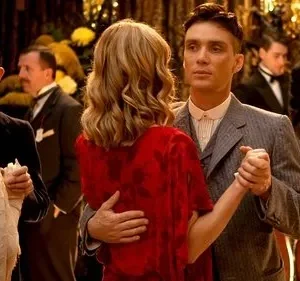 Casal elegante dança em festa dos anos 20/30. Ele de terno risca de giz, ela de vestido vermelho. Outros convidados e músico ao fundo.