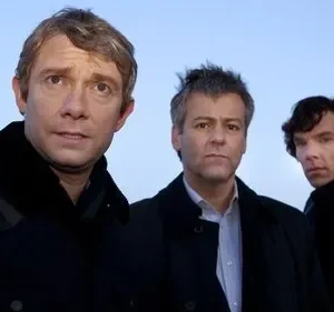 Três homens em casacos escuros. Um preocupado, dois sérios. Posam contra um céu azul pálido. Clima de mistério e investigação.