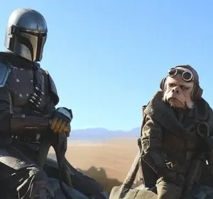 Figura blindada e alienígena com óculos em deserto árido sob céu azul. Clima de ficção científica e aventura.